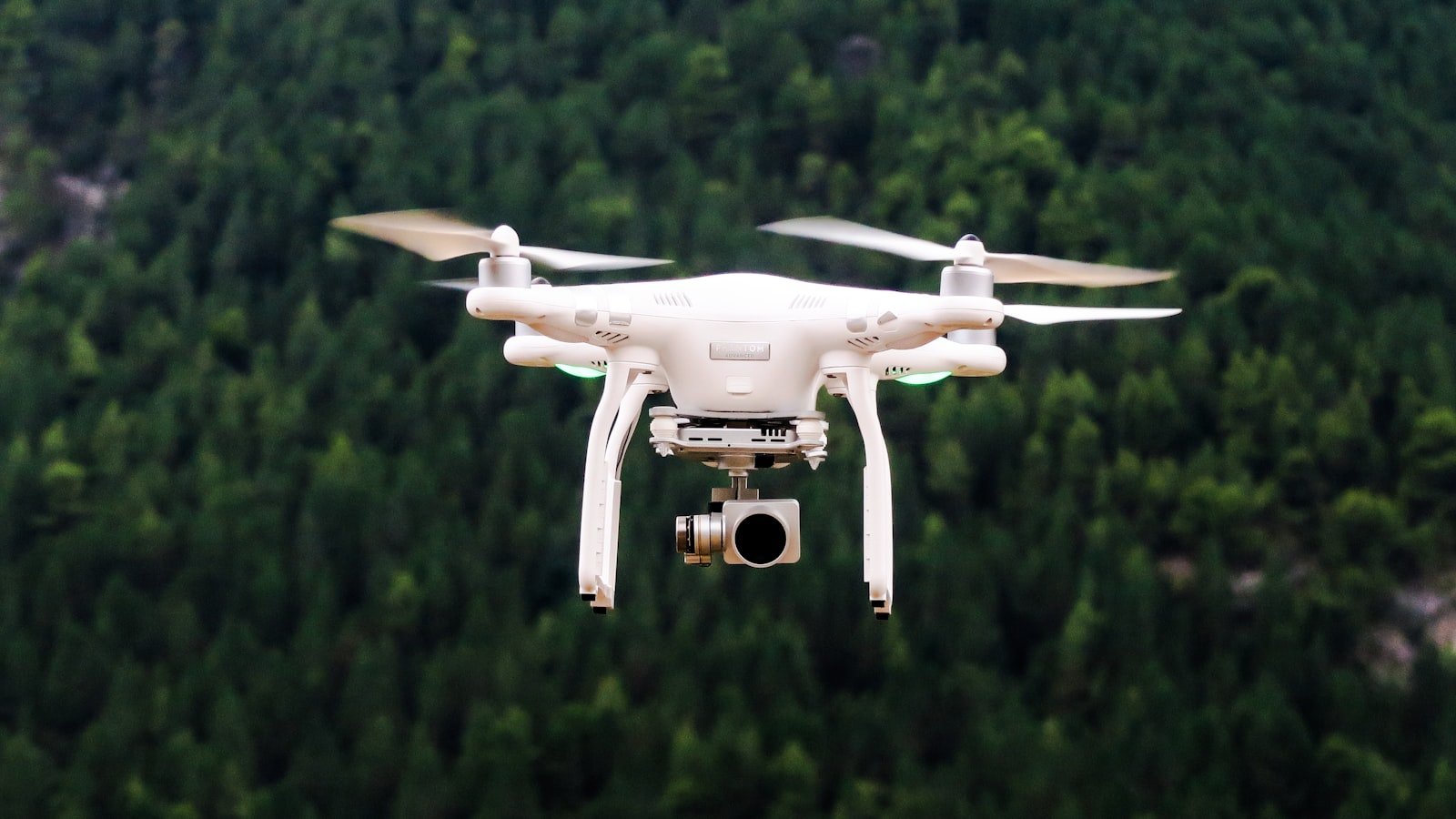 Quadcopter drone with camera gimbal flying over forested terrain